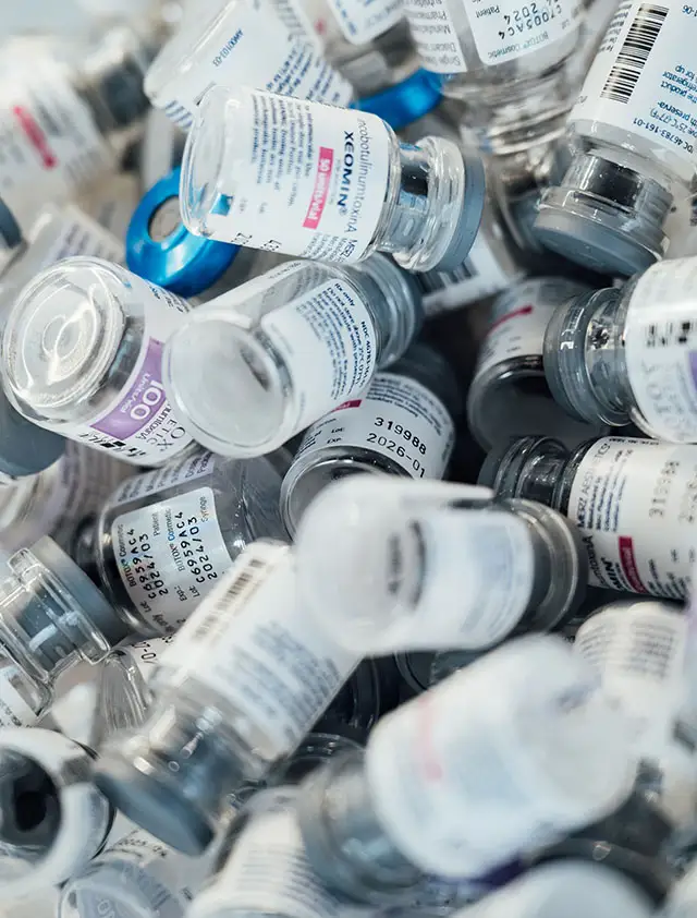 A close-up vertical shot of a large pile of empty glass medical vials, including some labeled Xeomin and Botox.